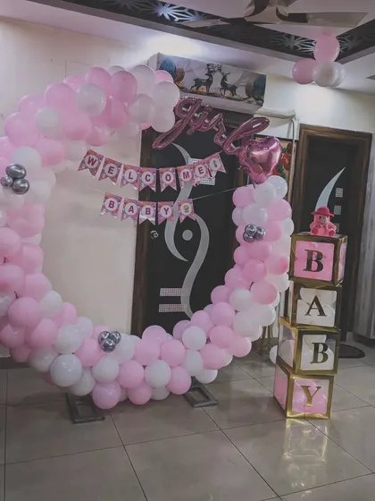 This welcome home setup for a baby girl features a full balloon ring in pink and white. The design is complemented by "It's a Girl" foil balloons and decorative "BABY" blocks for a complete look.