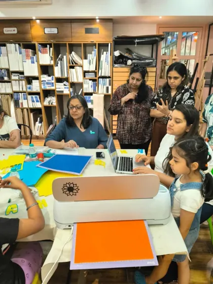 A group of mothers and children gathered around a Cricut machine, learning to craft personalized keychains in a special Mother's Day workshop.