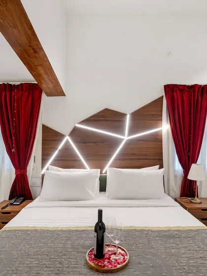 A modern bedroom with a unique, custom-designed headboard featuring geometric backlighting. The bold red curtains add a dramatic pop of color to the otherwise neutral and contemporary space.