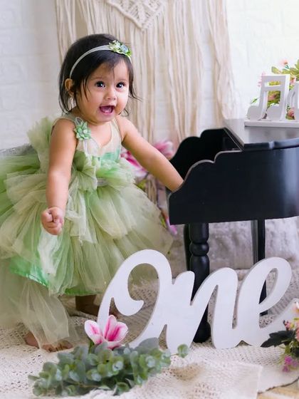 A moment of pure joy and excitement. This little girl in her green dress can't contain her happiness during her first birthday photoshoot.