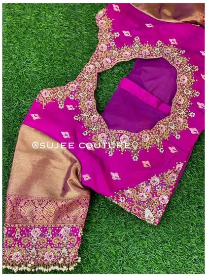 The back view of the magenta and gold blouse. It has a large circular cutout framed with intricate floral embroidery, combining traditional fabrics with a modern silhouette.