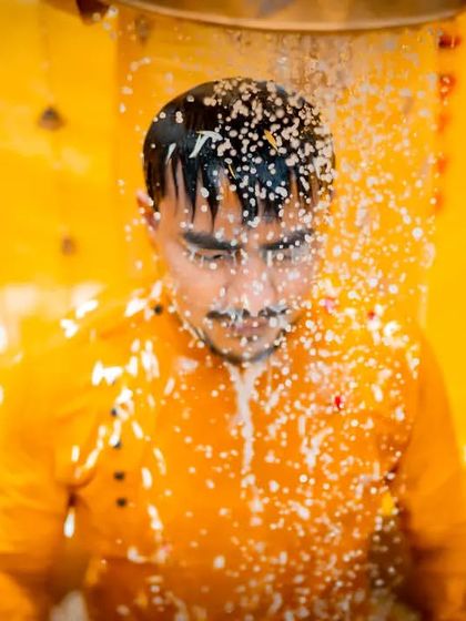 An action shot from a Haldi ceremony, capturing the moment the groom is doused with water and rice as part of the ritual.