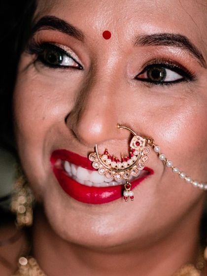 A close-up of a bride's joyful smile. Her bright red lipstick and traditional nose ring are the focus of this happy portrait.