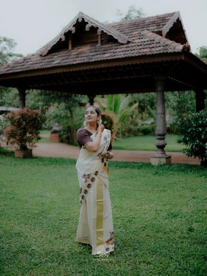 The bride looking up with a hopeful smile, standing in the garden of a traditional Kerala venue.