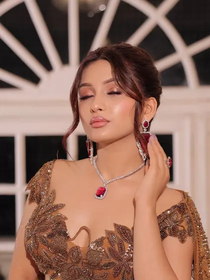 A serene, eyes-closed portrait, highlighting the flawless makeup and statement ruby necklace.
