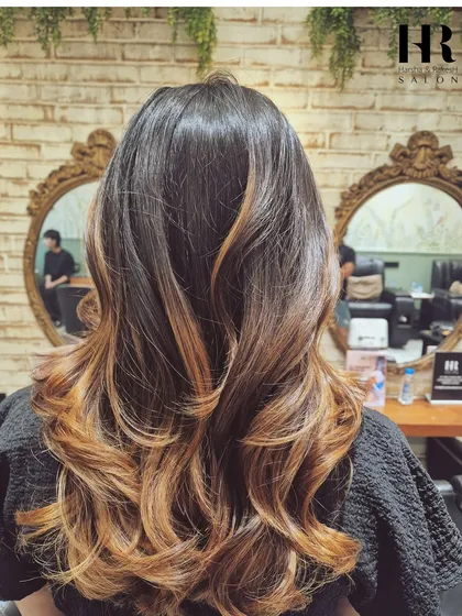 New hair, new you. This look features a beautiful transition from a dark root to lighter, caramel-toned ends, expertly blended and styled into glamorous waves for a truly transformative effect.