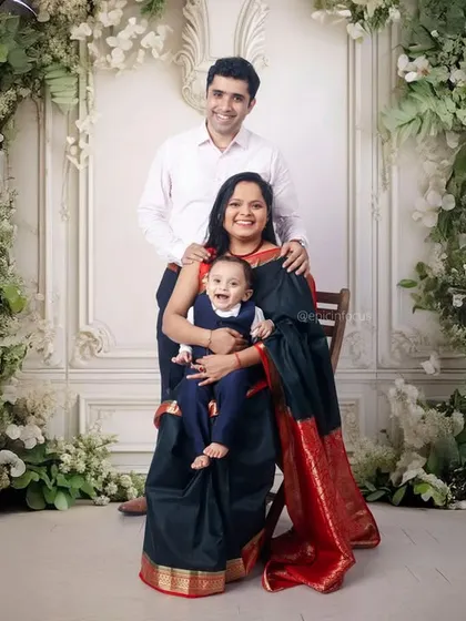 An elegant family portrait set against a grand, floral archway. The parents are dressed in traditional and formal wear, creating a timeless and sophisticated image.