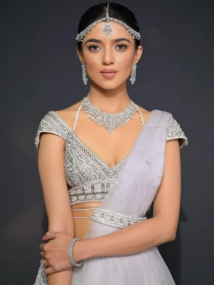 The front view of this modern bridal look. The hair is pulled back cleanly into a bubble ponytail, which allows the stunning matha patti and makeup to shine.