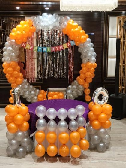 A circular balloon arch in orange and silver for a 10th birthday party. The setup includes a decorated table in the center, making it a perfect spot for cake cutting.