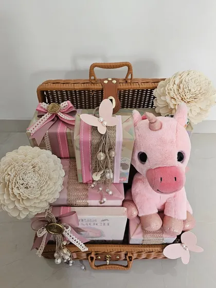 The full view of the pretty pink trunk hamper, complete with a unicorn plushie. The variety of wrapping styles and embellishments creates a rich, textured, and cohesive look.