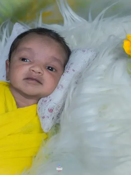 An awake newborn wrapped in bright yellow, looking up with curiosity. The soft fur and colorful flowers complete the cheerful scene.