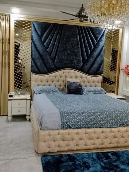 A master bedroom designed for pure luxury and comfort. The deep blue velvet headboard creates a dramatic focal point, complemented by a stunning crystal chandelier and custom mirrored panels, proving that a bedroom can be both a restful sanctuary and a statement of style.