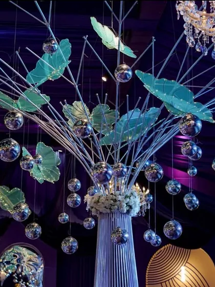 A unique centerpiece featuring a tree-like structure adorned with translucent green leaves and hanging silver disco balls. This piece perfectly blended natural forms with glamorous, party-ready elements.