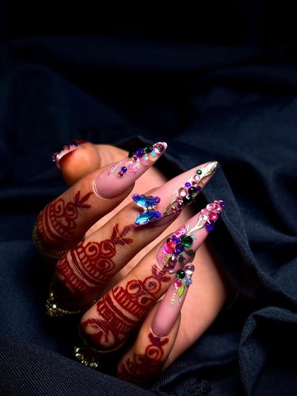 A close-up on the butterfly and floral nail art, showing the delicate placement of gems and charms.