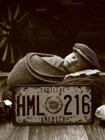 A vintage Route 66 inspired photoshoot. This sepia-toned image with classic car props and signs creates a timeless, nostalgic feel for a baby boy's portrait.