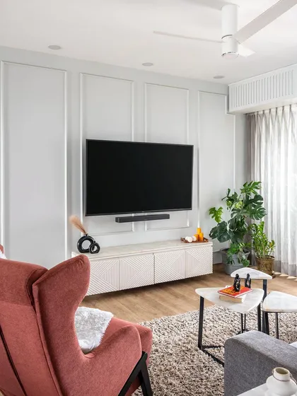 This cozy living room was designed for a calm and timeless feel. The neutral wall with classic molding, a textured TV unit, and a pop of color from the rust-red armchair create a balanced and inviting atmosphere.