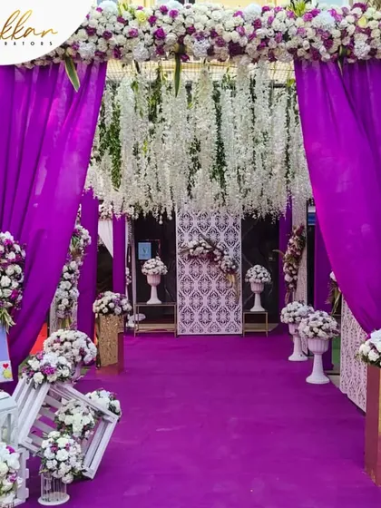 A bold and contemporary entrance design. The vibrant purple carpet and drapes, combined with hanging white floral strings, create a striking and modern look.