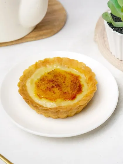 A side view of the crème brûlée tart, showing the flaky crust and creamy filling. This angle provides more detail for customers browsing a dessert menu.
