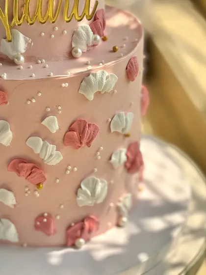 A close-up detail of the pink first birthday cake, showing the texture of the palette-knife buttercream petals and the scattered edible pearls.
