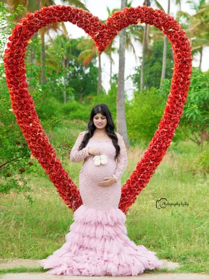 A beautiful outdoor portrait of a mother-to-be holding tiny baby shoes in front of our red floral heart prop.