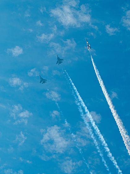 Three fighter jets in formation, leaving long trails of smoke against a blue sky.