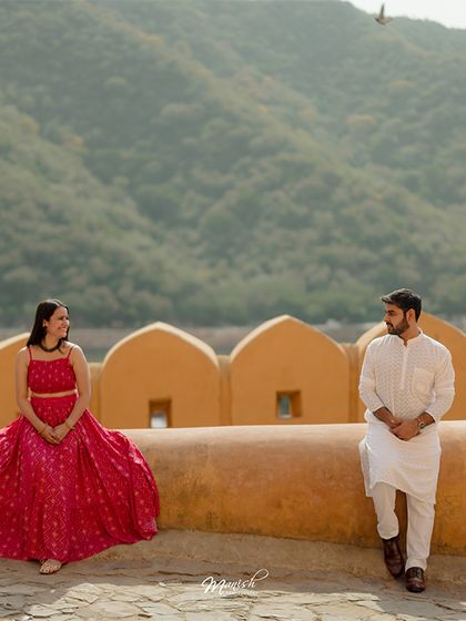 A beautifully composed shot on the fort walls, with the Aravalli hills in the background, showcasing the grandeur of a Jaipur pre-wedding shoot.