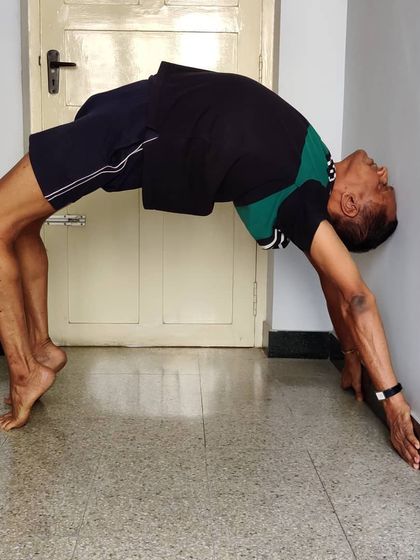 Chakrasana (Wheel Pose) or Urdhva Dhanurasana, performed against a wall. The wall provides support to walk the hands down, building strength and confidence for the full backbend.