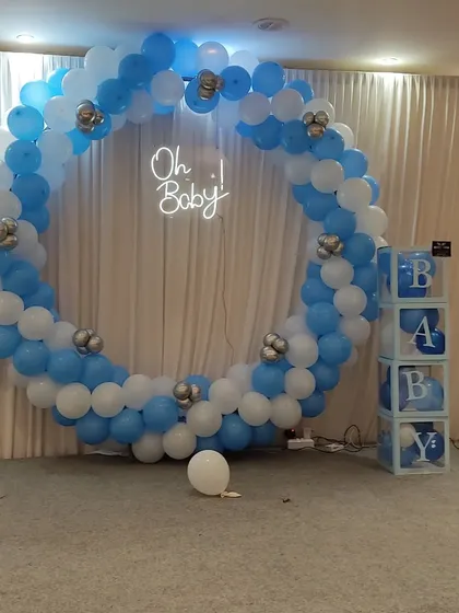 A full circular balloon frame in blue and white for a baby shower, with an "Oh Baby" neon sign and "BABY" blocks.