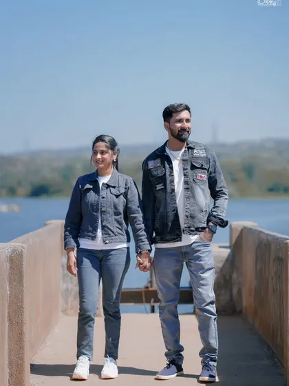 A casual and happy photo of the couple walking hand-in-hand on a pier. Their coordinated denim outfits look great against the water.