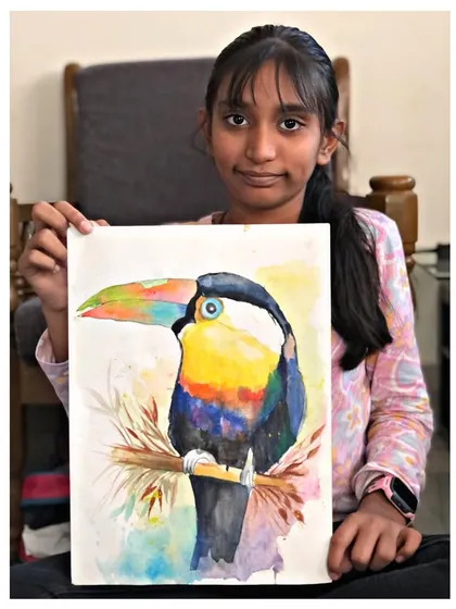A student holds her beautiful watercolour painting of a toucan. The wet-on-wet technique gives the background a soft, dreamy feel.