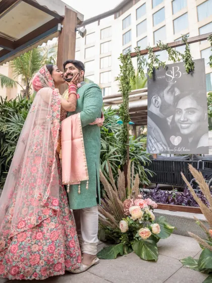 A playful and sweet moment as the bride gives the groom a kiss on the cheek. The custom wedding signage in the background adds a personal touch to this lovely candid shot.