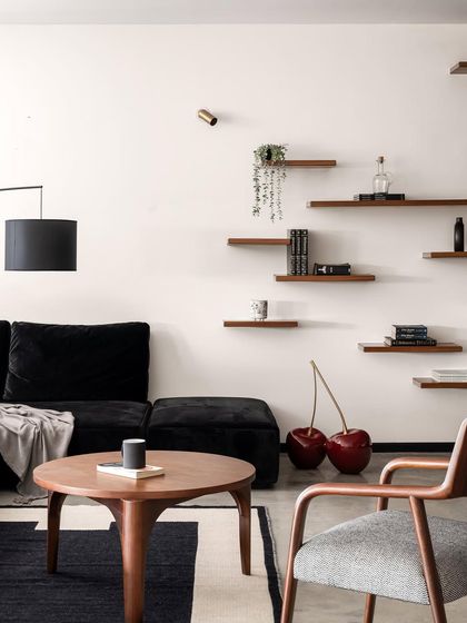 A quirky detail in the Ebony & Ivory living room, where a giant cherry sculpture adds a pop of color and personality. The space features a custom black sofa, a walnut coffee table, and a modern armchair.