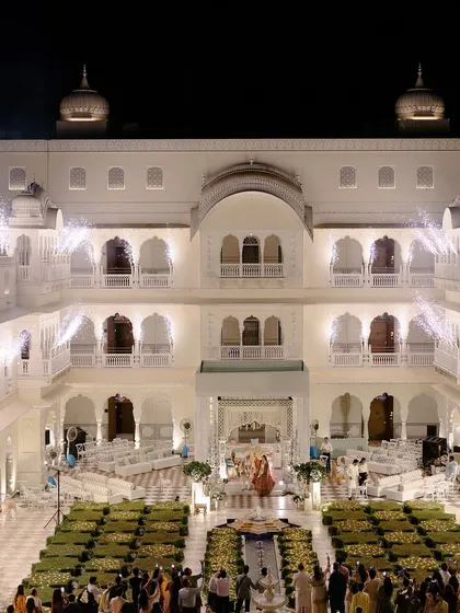 A wide-angle shot of the wedding ceremony at night, with the entire palace lit up and fireworks in the background.