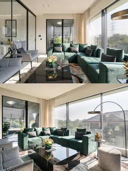The living area in Residence 100 features a bold emerald green sectional sofa, adding a vibrant pop of color against the neutral palette and large glass windows.