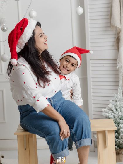 A joyful mother and son wearing Santa hats and sharing a laugh.