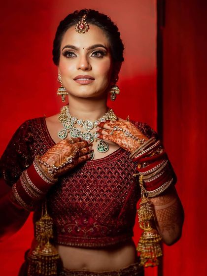 A stunning bridal portrait of Shubhangi against a dramatic red backdrop. Her makeup looks flawless and her expression is captivating.