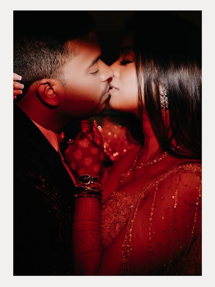 An intimate, close-up kiss between Aabhaas and Radhika, bathed in dramatic red light. This image is passionate and cinematic, capturing the intensity of their connection during their engagement party.