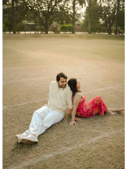 A relaxed and casual pose with the couple sitting back-to-back in an open field, enjoying a quiet moment together.