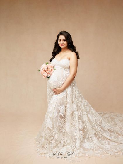 Holding a bouquet of pink flowers, this mother-to-be looks serene and beautiful in a strapless white lace gown.