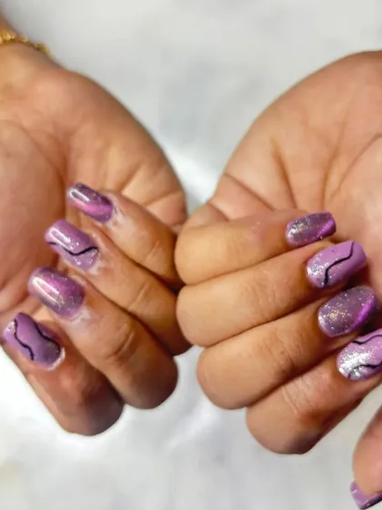 A fun design on shorter square nails. This set features a shimmery purple cat-eye base with hand-painted abstract black lines and a touch of glitter.