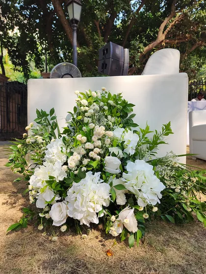 A beautiful ground-level floral arrangement of fresh white hydrangeas, roses, and greenery. This type of decor is perfect for lining an outdoor aisle or decorating the base of a stage.