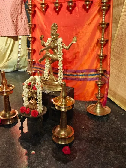 A sacred space is created on stage with a statue of Lord Nataraja and traditional lamps, setting a divine atmosphere for a classical dance performance.