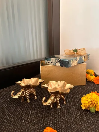 A pair of golden elephant-shaped T-light holders. These are a charming addition to any festive decor and make for a wonderful return gift.