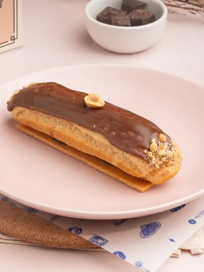 The Hazelnut Eclair, showcasing its smooth milk chocolate glaze and a single hazelnut as a garnish.