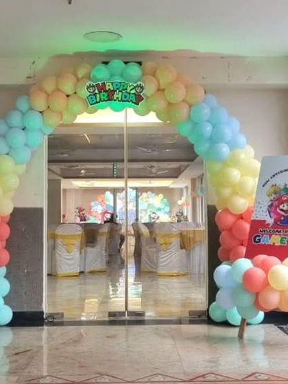 A pastel-colored balloon arch and welcome signs for a Mario-themed joint birthday party.