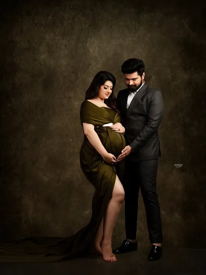A sophisticated and intimate couple portrait against a dark, painterly backdrop. The contrast between her olive green gown and his dark suit creates a rich, elegant look.