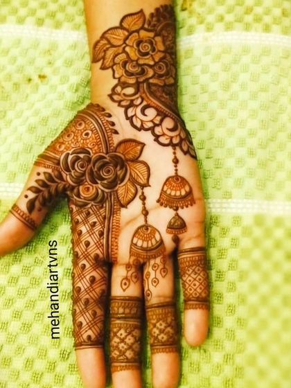 A delicate and modern design featuring roses and hanging jhumkas (earrings). This style is perfect for a festive occasion or a housewarming (Grihpravesh).