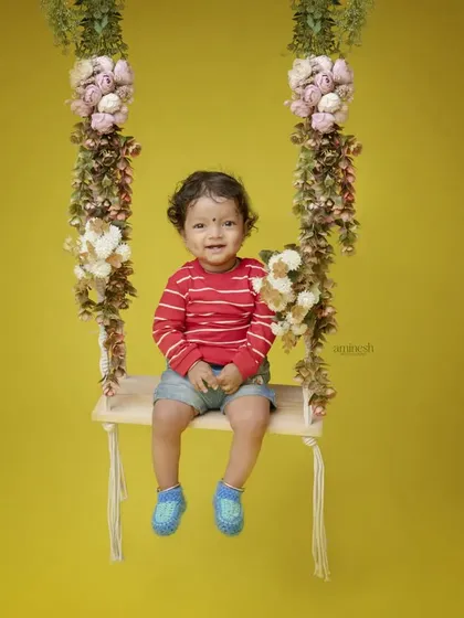 A simple, bright, and happy portrait of a baby on a floral swing against a solid yellow background. Sometimes the simplest setups create the most beautiful memories.