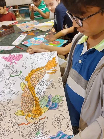 A student proudly shows his progress on his lucky carp drawing. You can see the intricate scales he has started to color, a testament to his patience and skill.
