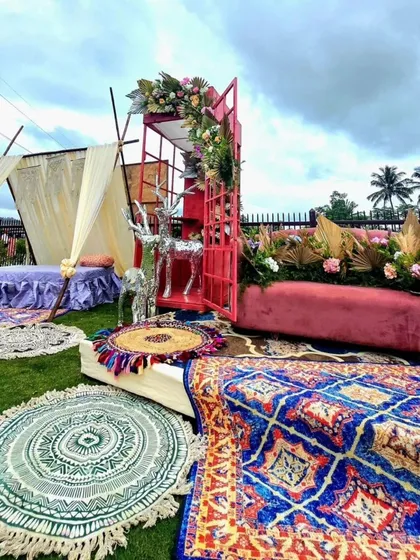 A bohemian-chic outdoor seating area. The setup includes low seating on colorful rugs, a teepee tent, and a velvet sofa, creating a relaxed and stylish vibe.